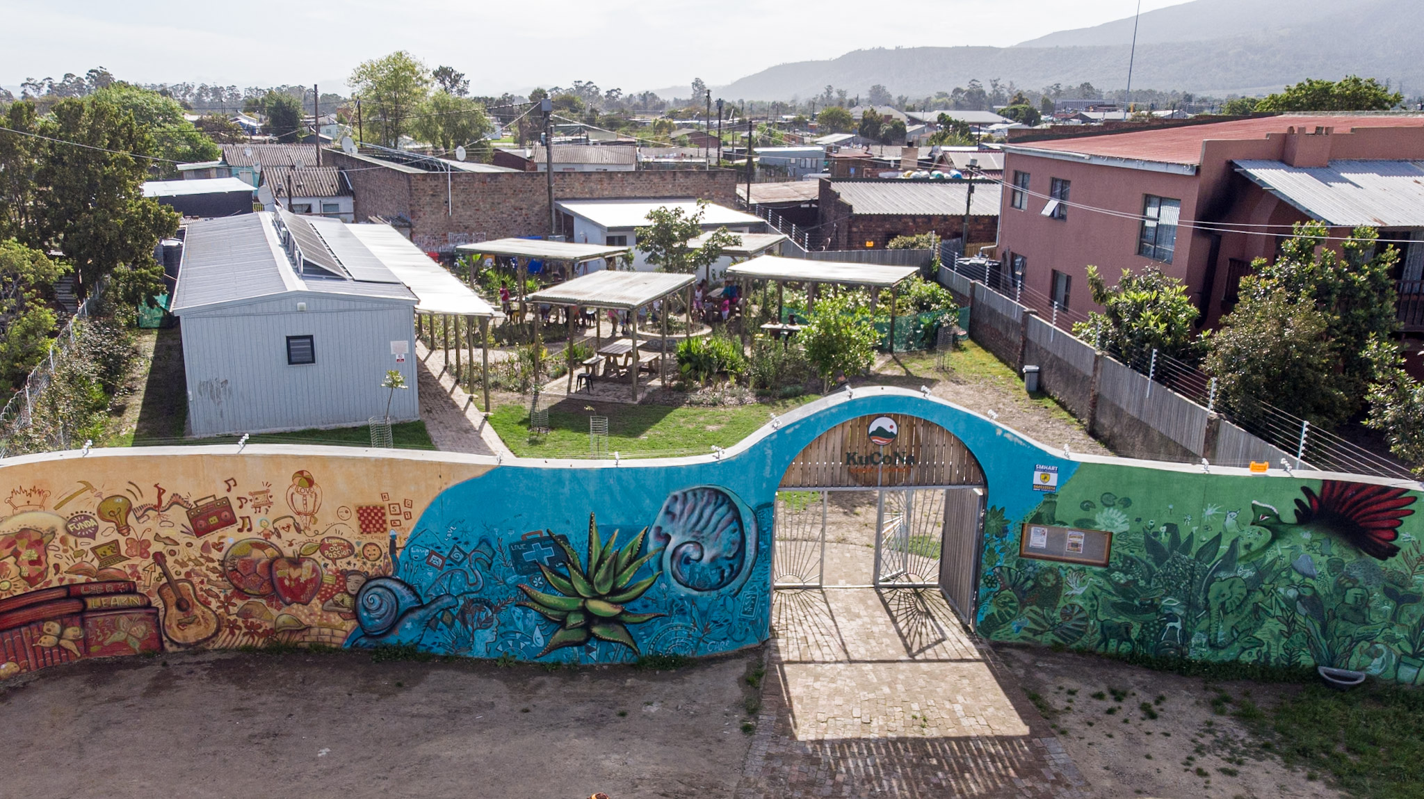 Aerial view of the KuCoNa centre behind its colourful mural wall and entrance gate