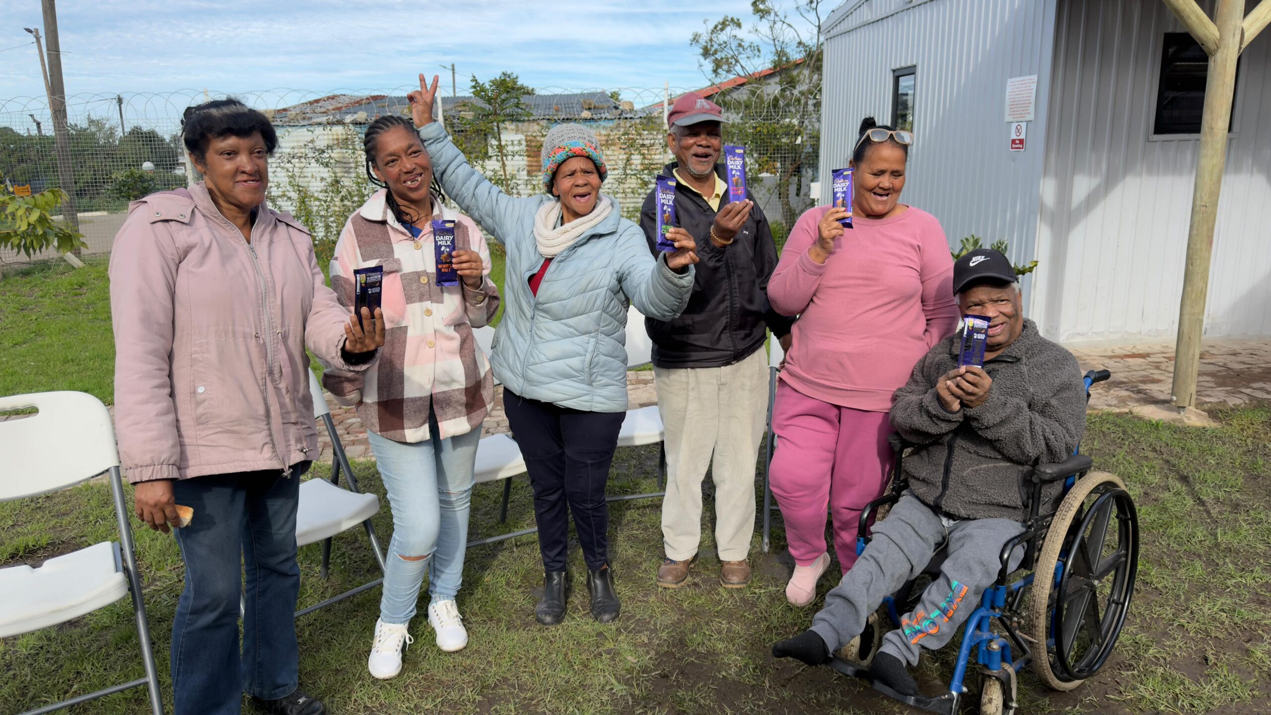 Smiling seniors outside the centre holding up chocolate prizes, one cheering with a peace sign