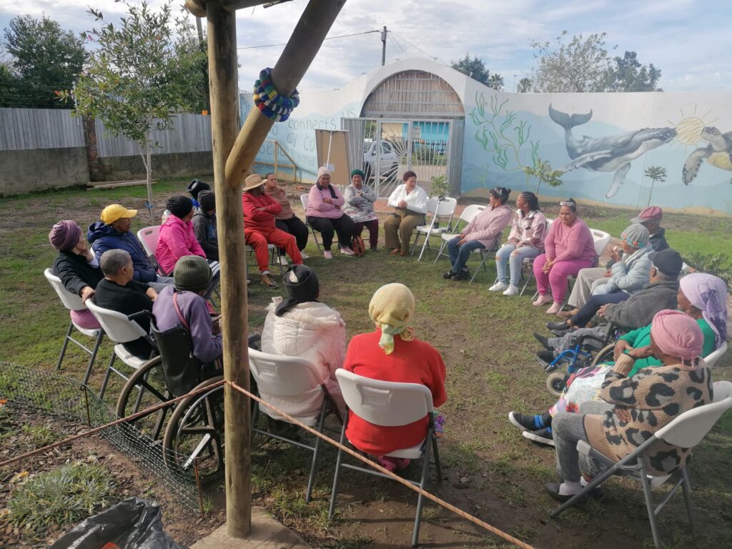 Seniors sitting in a circle on the lawn in front of the KuCoNa mural