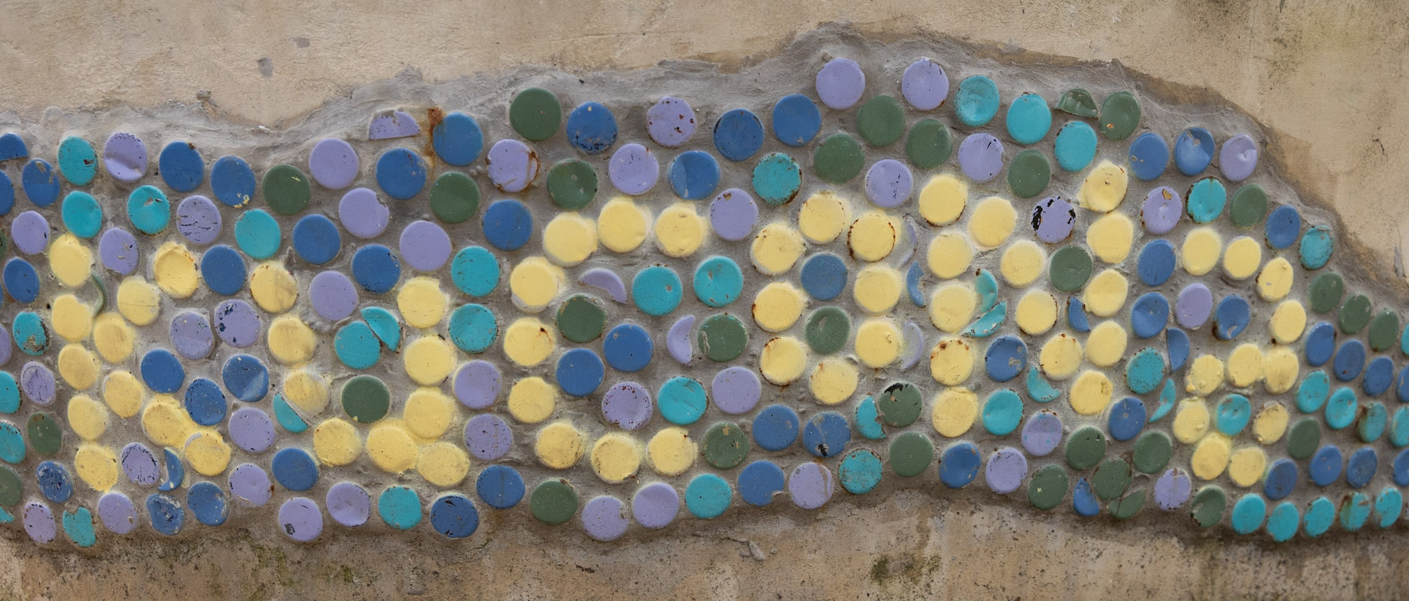 Mosaic of colourful bottle caps set into a plastered wall