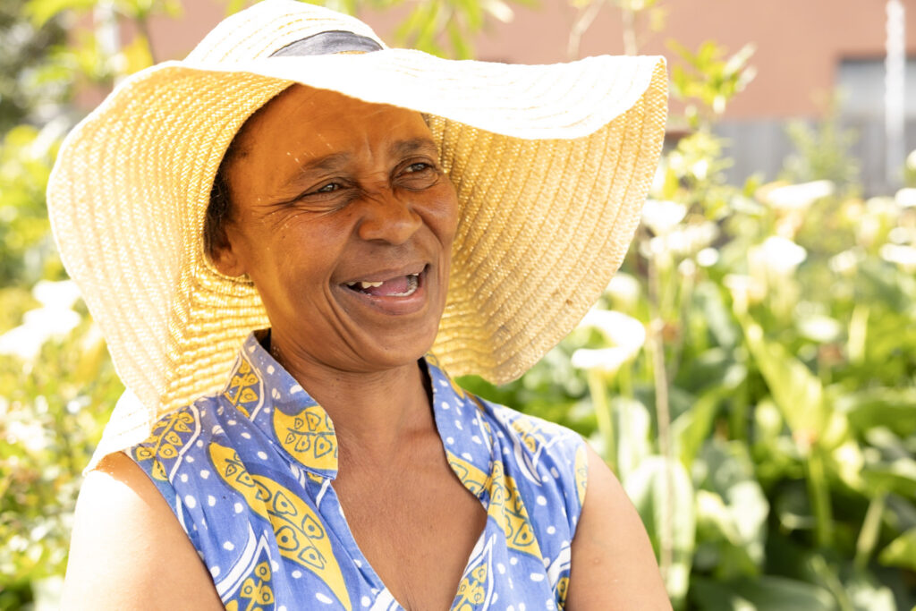 A smiling woman in a wide straw sun hat in the KuCoNa garden