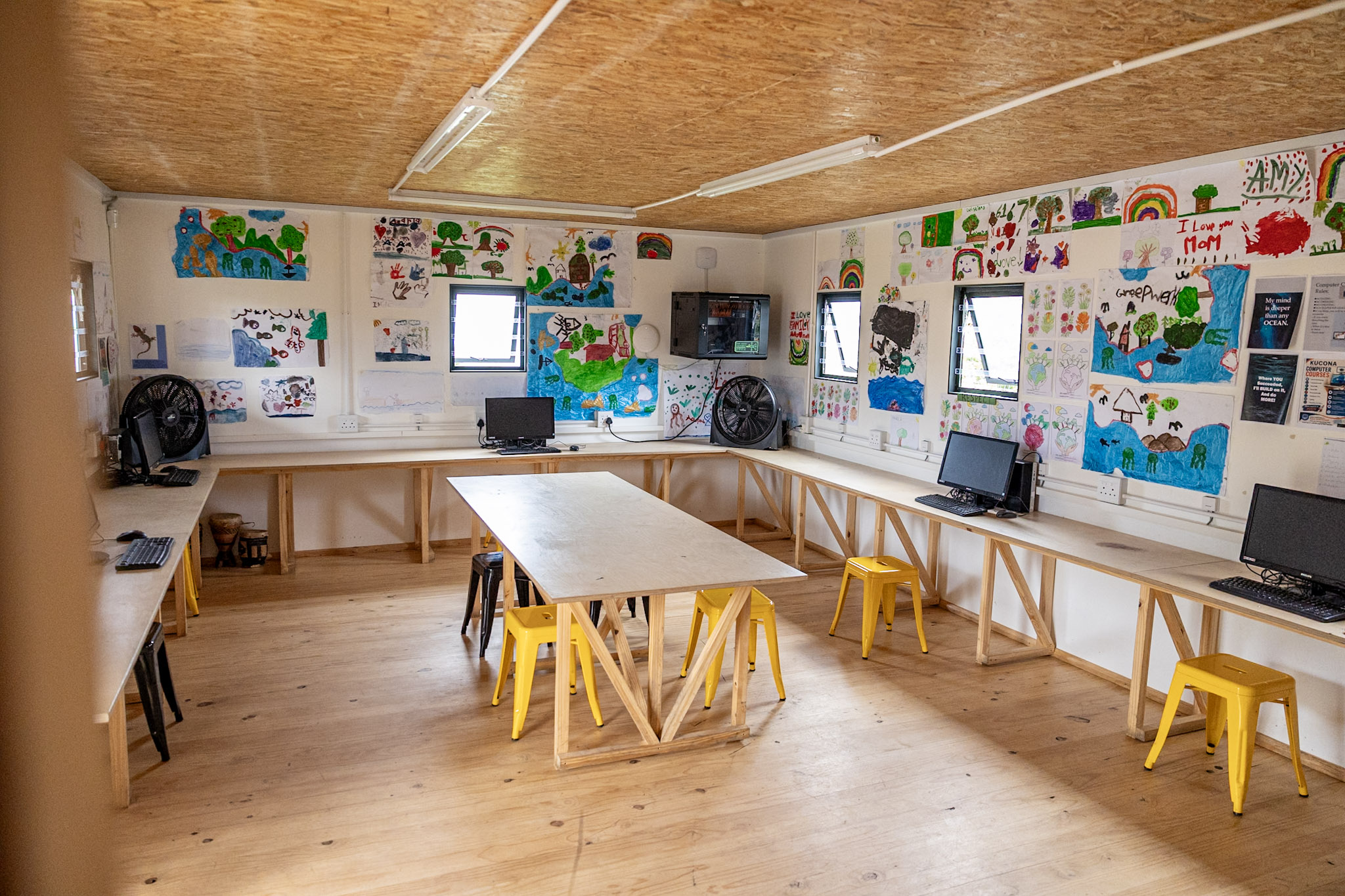 The Learning Hub classroom with computers, yellow stools and children’s artwork on the walls