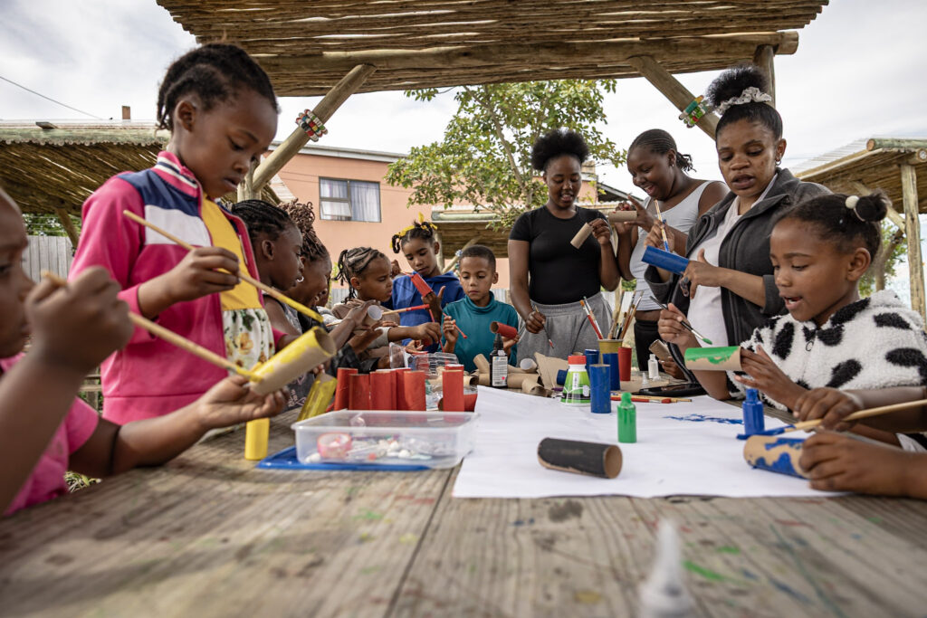 Children painting cardboard tubes at an outdoor craft table