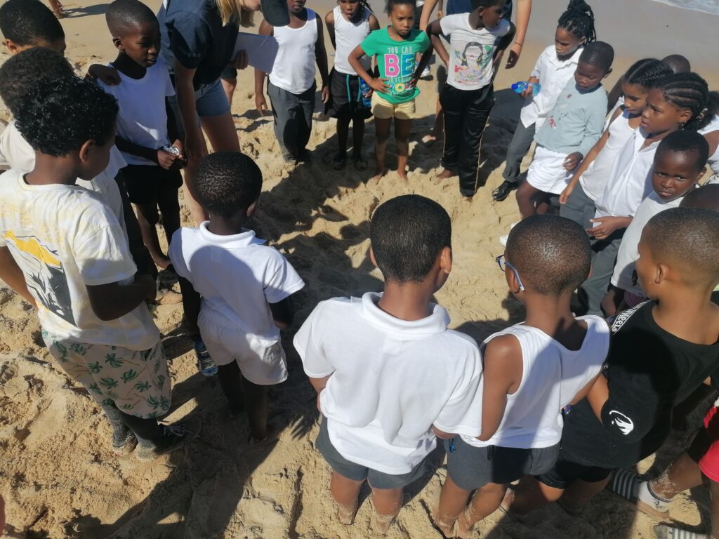 Children standing in a circle on the sand during a beach activity