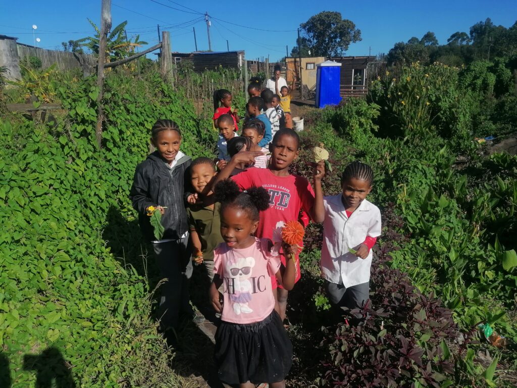 Children holding flowers on a path through a vegetable garden