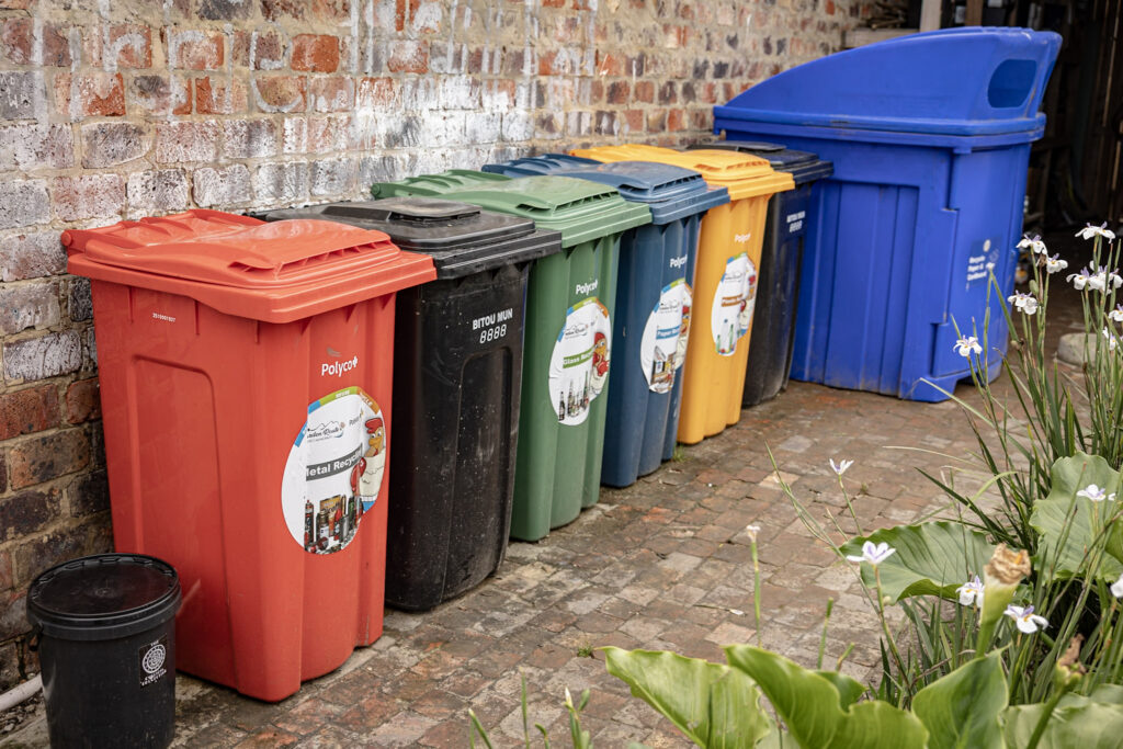 Colour-coded recycling bins lined up against a brick wall at the centre