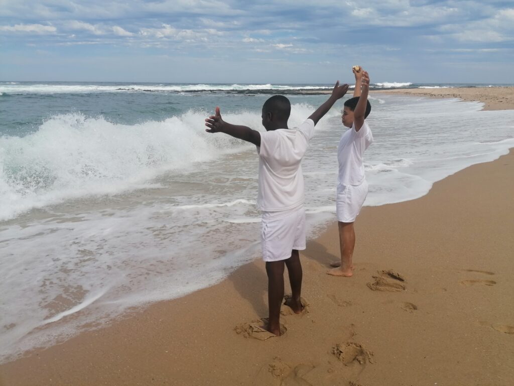 Two children with their arms raised at the water’s edge