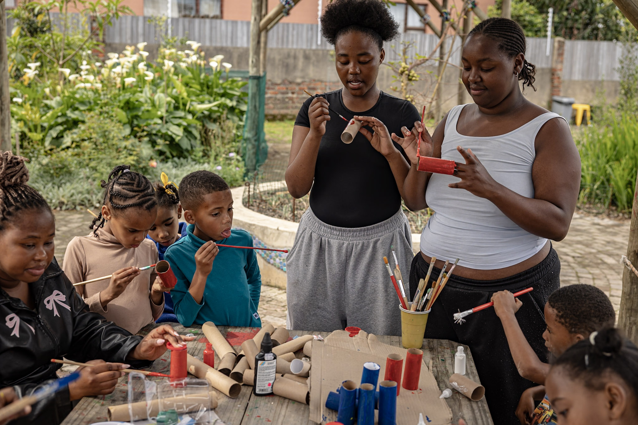 Young volunteers and children painting cardboard tubes at an outdoor craft table